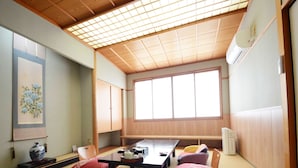A traditional Japanese room with tatami flooring, a low table, cushions, and a large window. - Hanagoyomi (Nanao)