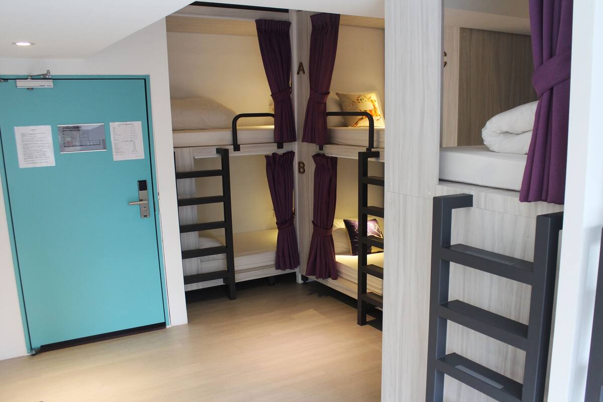 A dormitory room with bunk beds, a teal door, and a wooden floor.