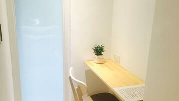 A small, narrow room with a wooden desk, a white chair, and a small potted plant.