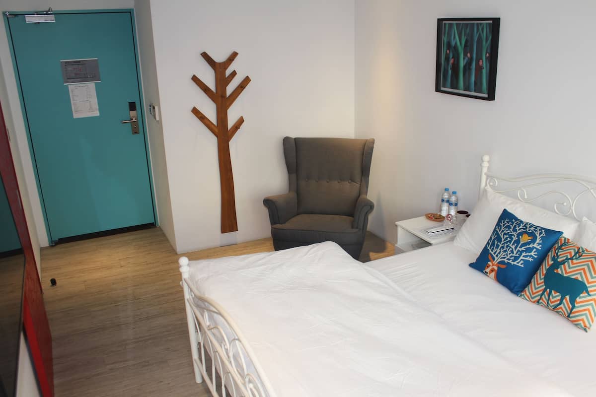 A hotel room with a bed, a chair, a nightstand, a wall-mounted picture, and a door.