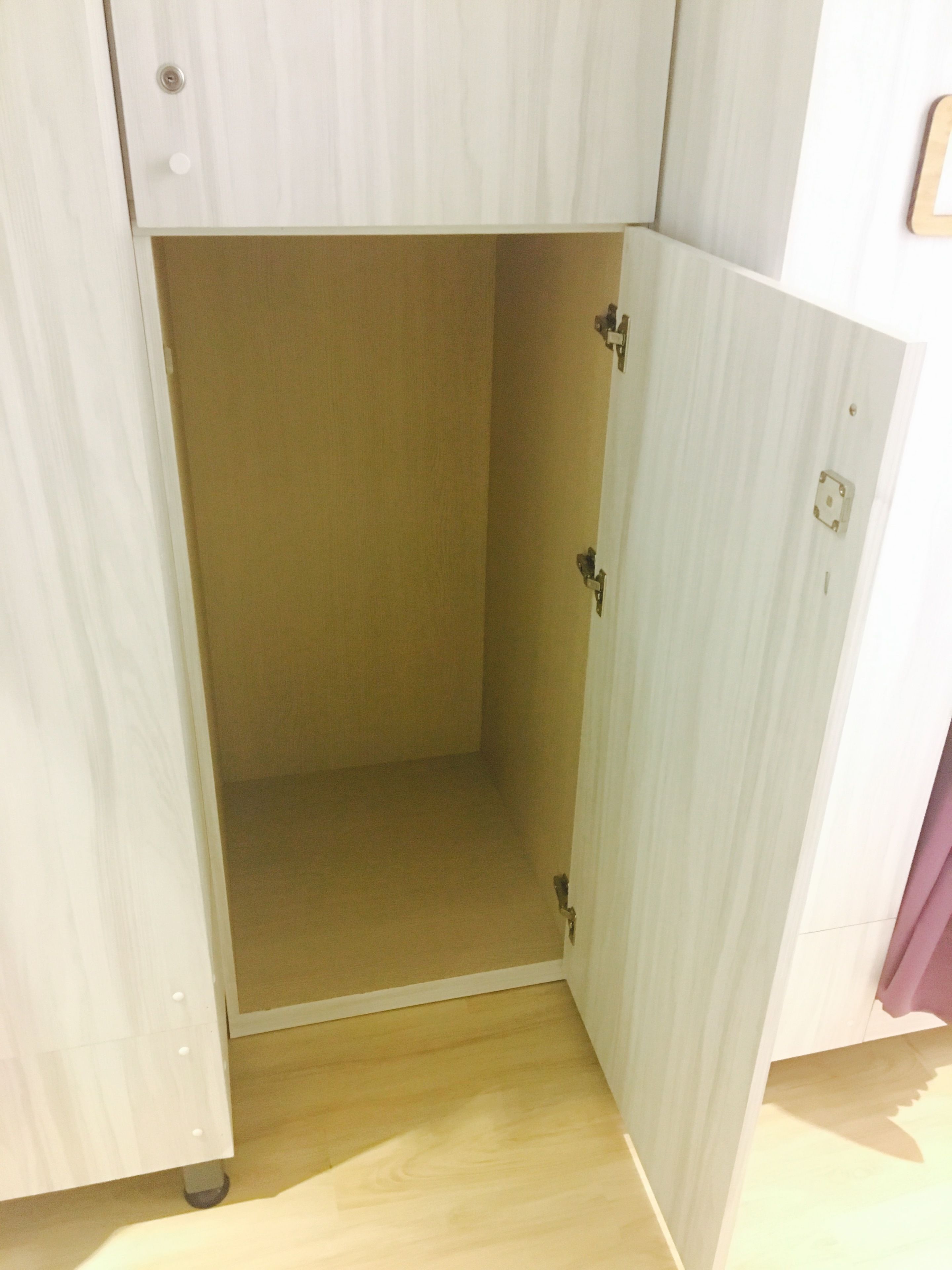 A room with a wooden cabinet with a single door, a light-colored floor, and a small shelf unit.