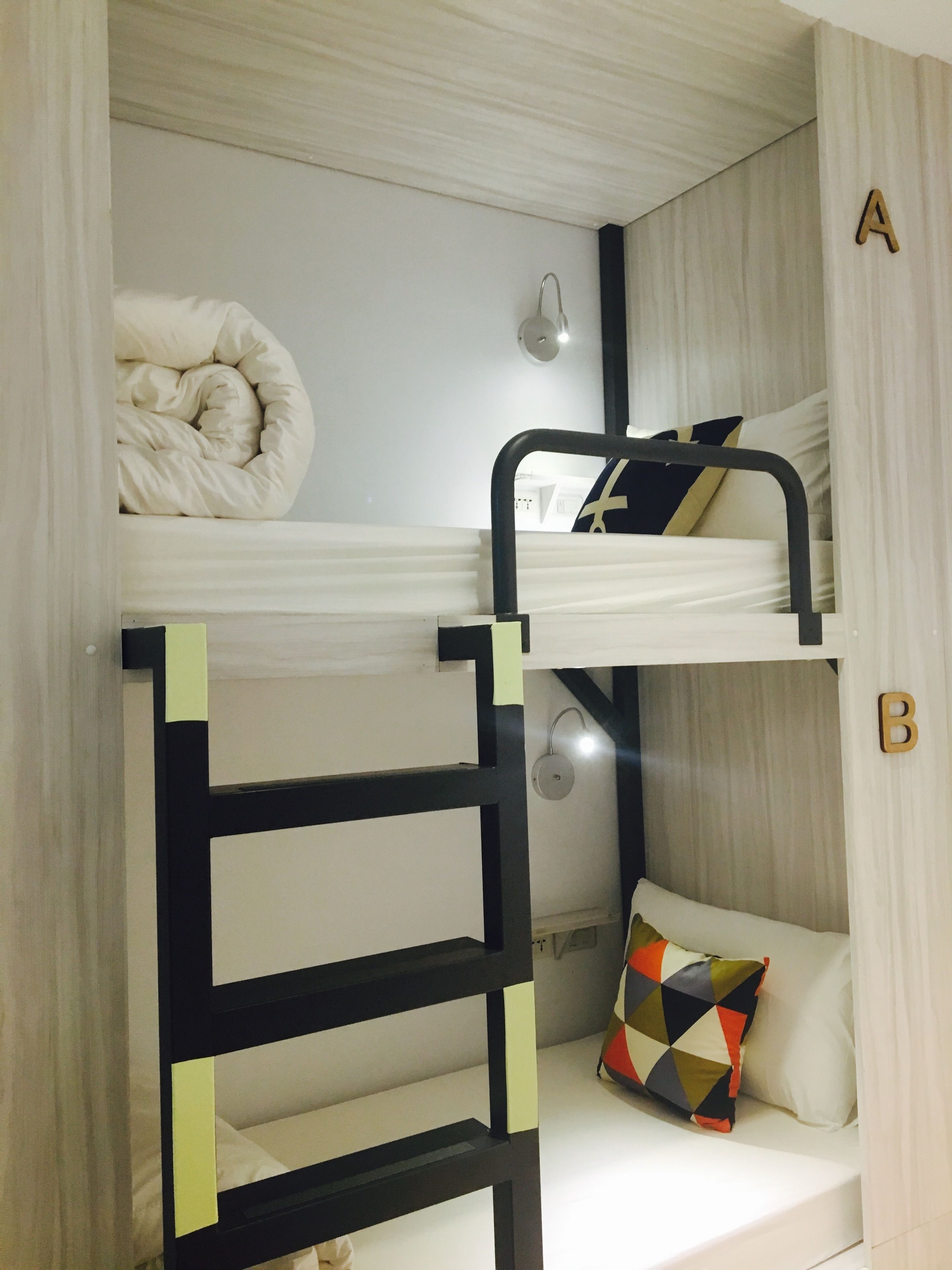 A bunk bed with a ladder, a pillow with a geometric pattern, and a wall-mounted light fixture.