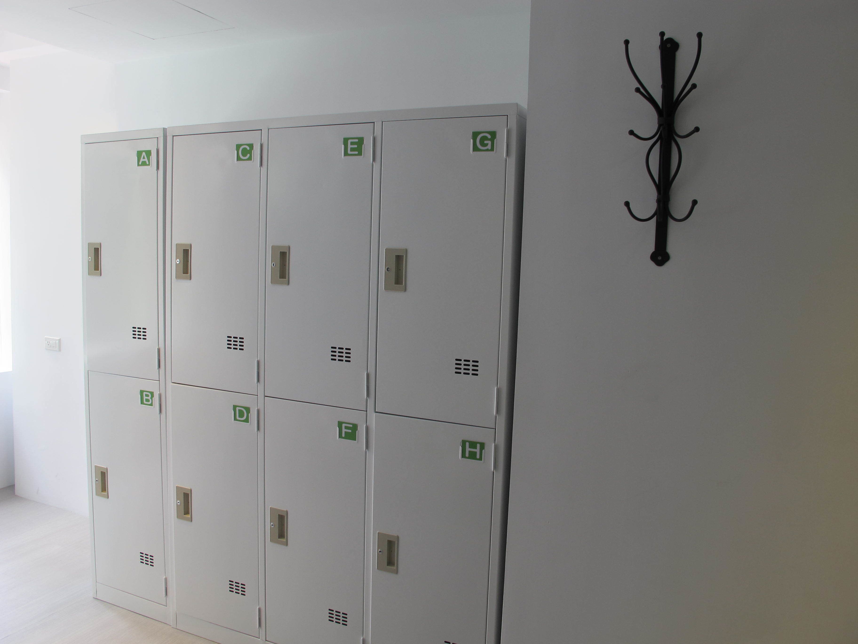 A row of white lockers with green labels, a black coat rack, and a light-colored floor.