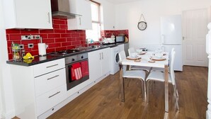 Une cuisine moderne avec des meubles blancs, un plan de travail recouvert de carreaux rouges, un four encastré et un coin repas avec une table et des chaises blanches.