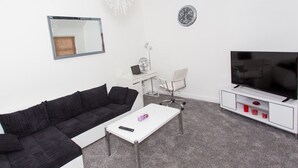Un salon moderne avec un canapé noir, une table basse blanche et un téléviseur posé sur un meuble blanc.