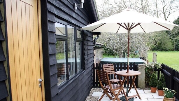 A patio with a table and chairs, a wooden door, and a black exterior wall. - Riverside House (Norwich)