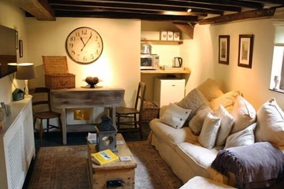 A cozy living room with a sofa, a wooden coffee table, a dining table, and a kitchen area in the background.