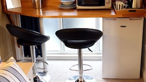 A compact kitchen with a microwave, a small refrigerator, and two bar stools. - Riverside House (Norwich)
