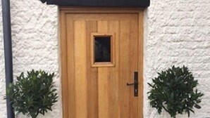 A wooden door with a small window, flanked by two potted plants. - Riverside House (Norwich)