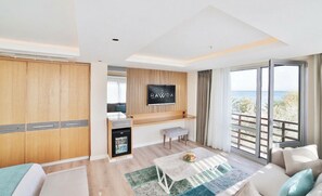 A modern hotel room with a kitchenette, a flat-screen TV, a sofa, a dining table, and a balcony with a view. - Rawda Resort Hotel Altinoluk (Edremit)