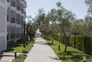 A pathway flanked by neatly trimmed hedges and trees, leading to a multi-story building with balconies. - Rawda Resort Hotel Altinoluk (Edremit)