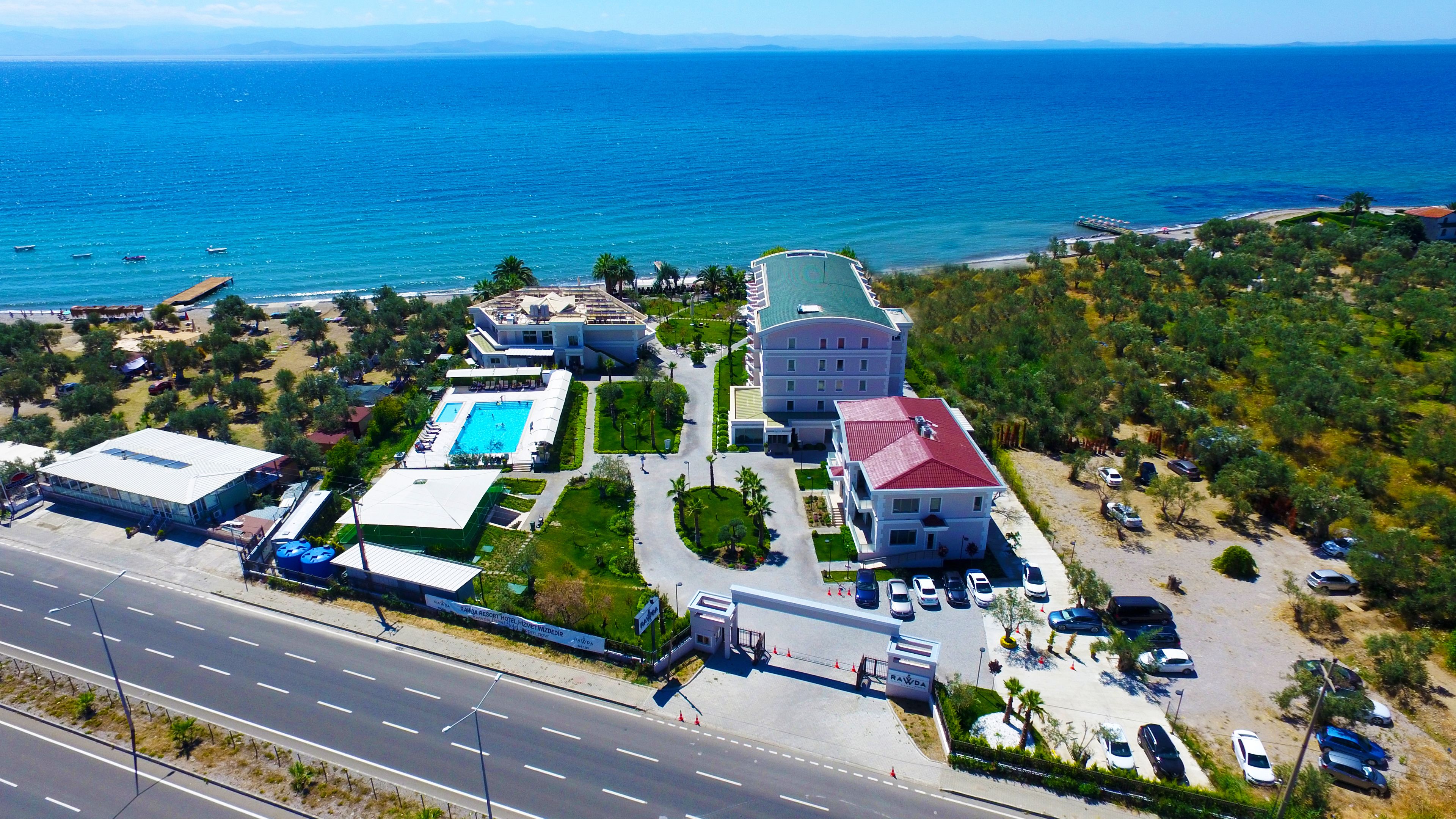 An aerial view of a resort with a swimming pool, a parking lot, and a view of the sea.