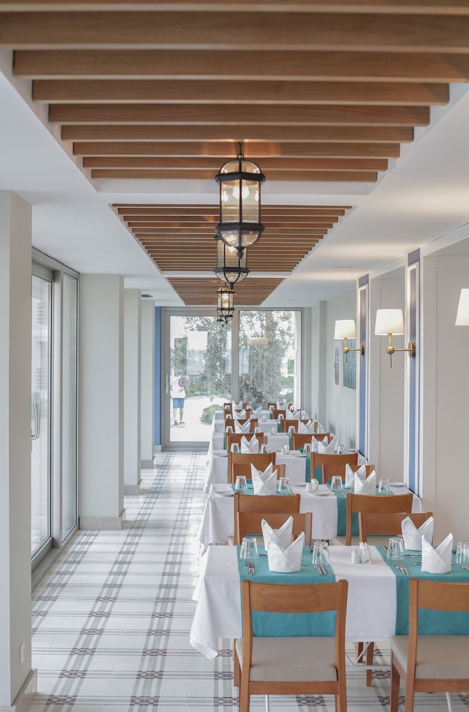 Un espace repas avec des tables dressées pour le service, un plafond avec des lambris en bois et une vue à travers les portes vitrées.