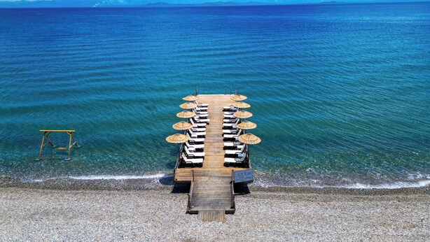 A wooden deck with lounge chairs and umbrellas, leading to a pebble beach. - Rawda Resort Hotel Altinoluk (Edremit)