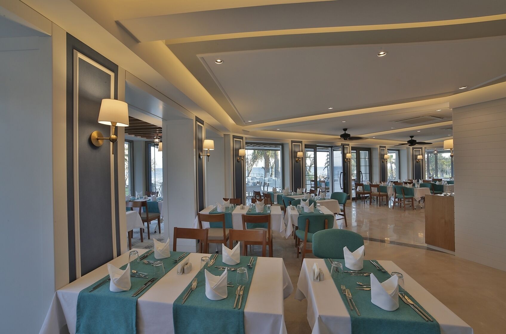 A spacious restaurant with multiple tables, each set with white tablecloths and green napkins.