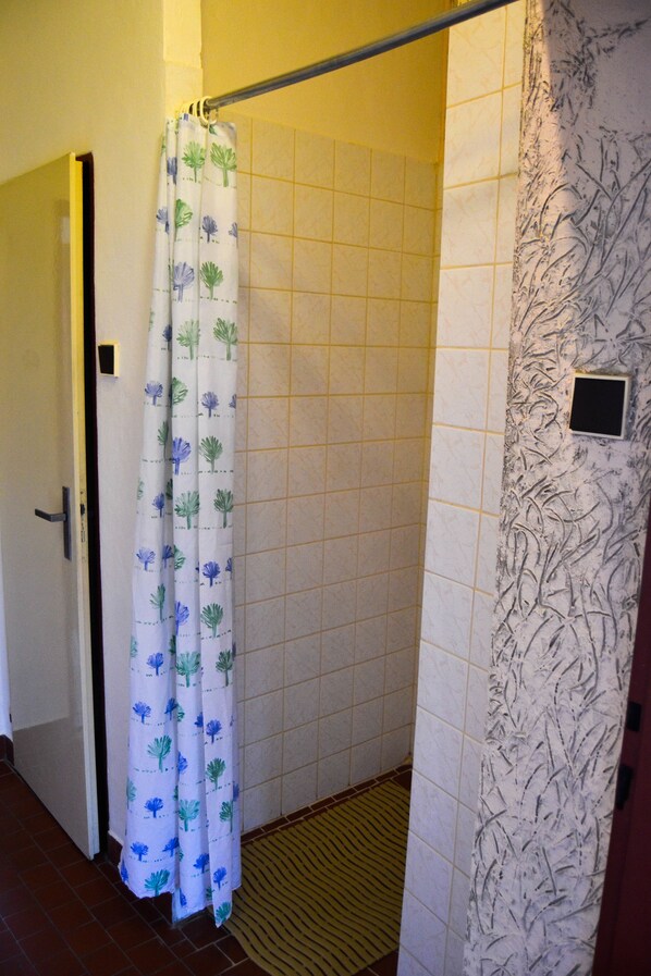 A shower area with a white curtain featuring blue and green patterns, tiled walls, and a textured wall on the right.