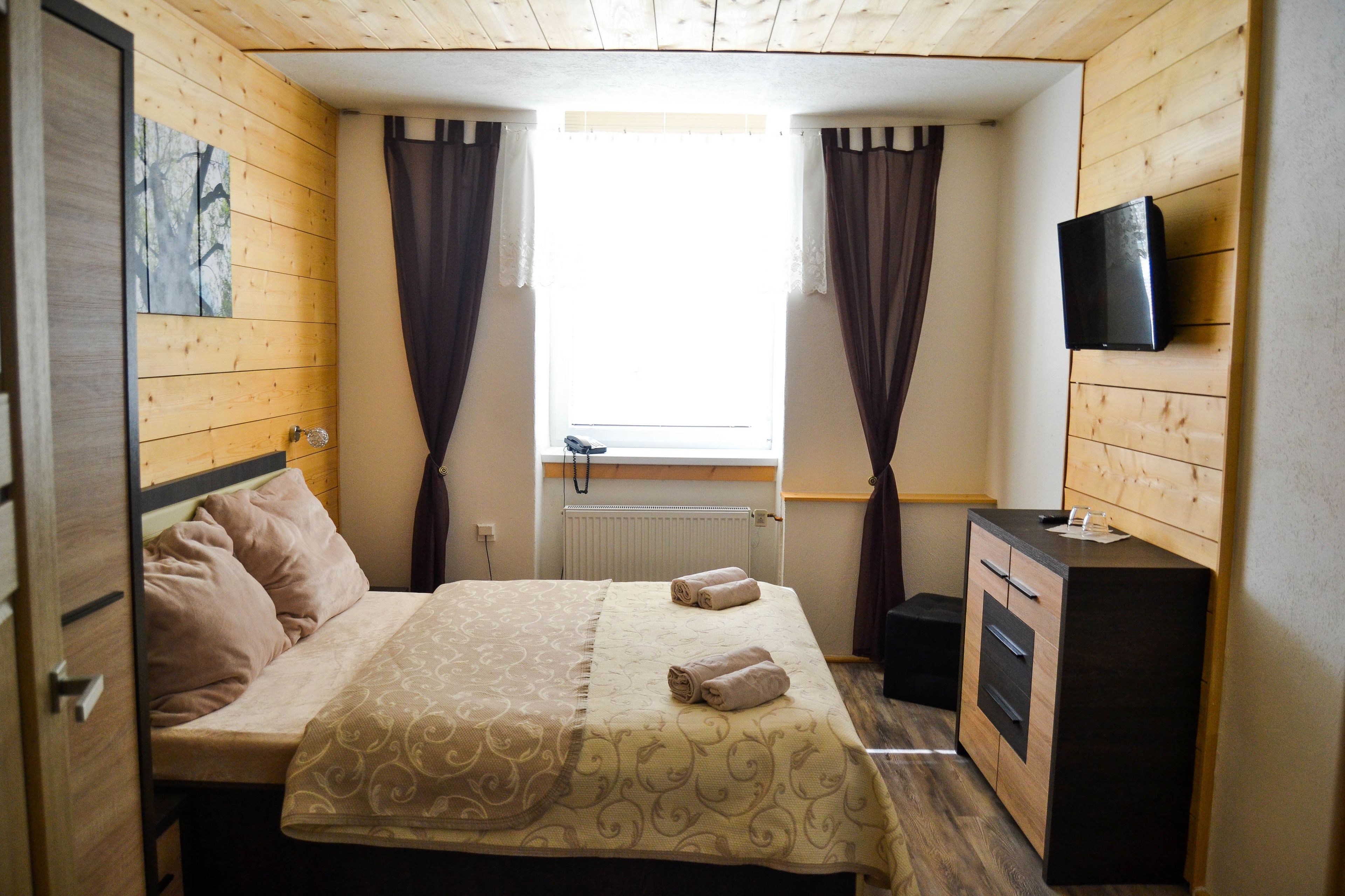 Una habitación pequeña con cama, televisión, ventana con cortinas y radiador.