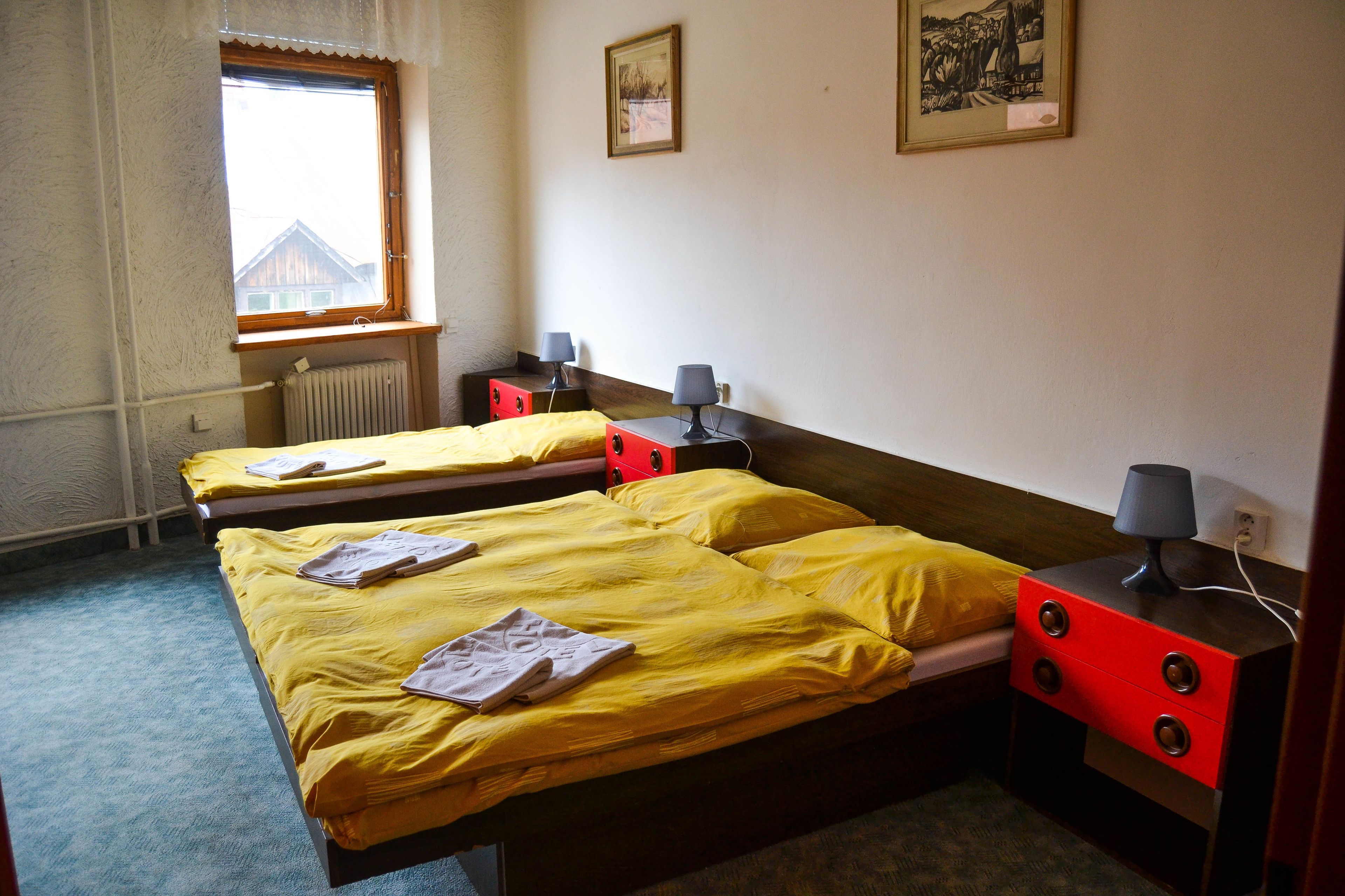A hotel room with two single beds, a red nightstand, a window, and a radiator.