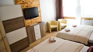 Habitación de hotel con dos camas, un televisor montado en una pared de madera, un escritorio con cajones y dos sillas.