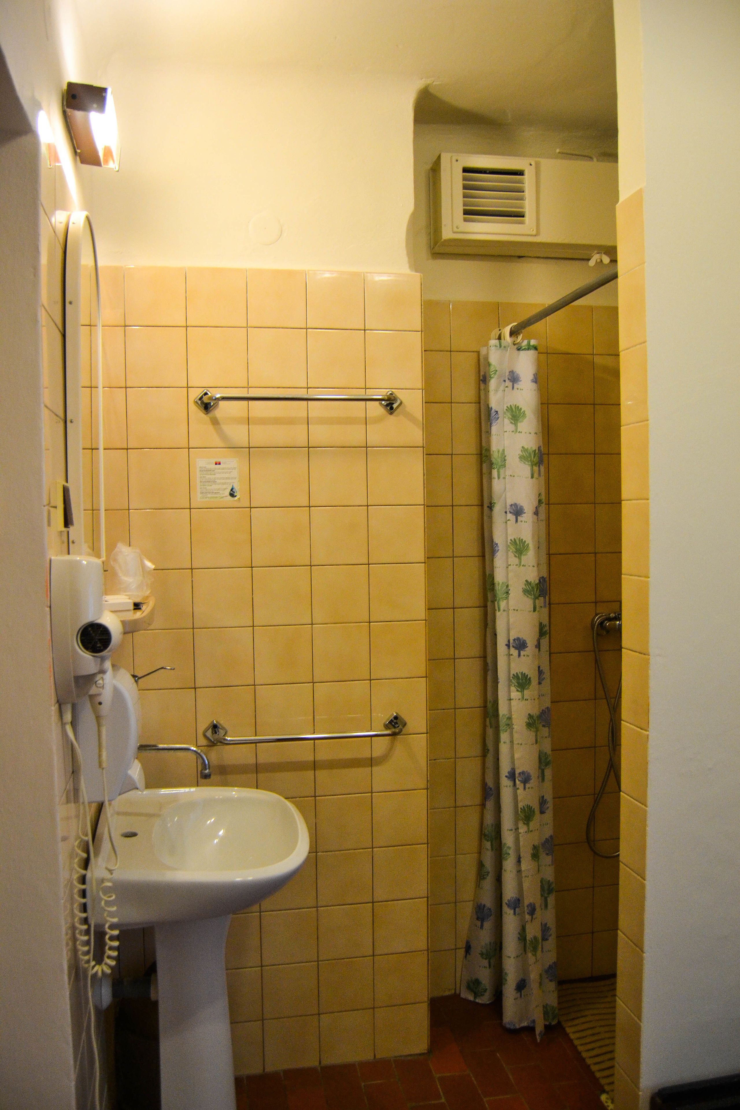 Une salle de bain avec des carreaux jaunes, un lavabo blanc, un porte-serviettes, un rideau de douche et un appareil de climatisation.