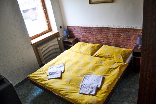 A hotel room with a bed, two bedside tables, a window, and a radiator.