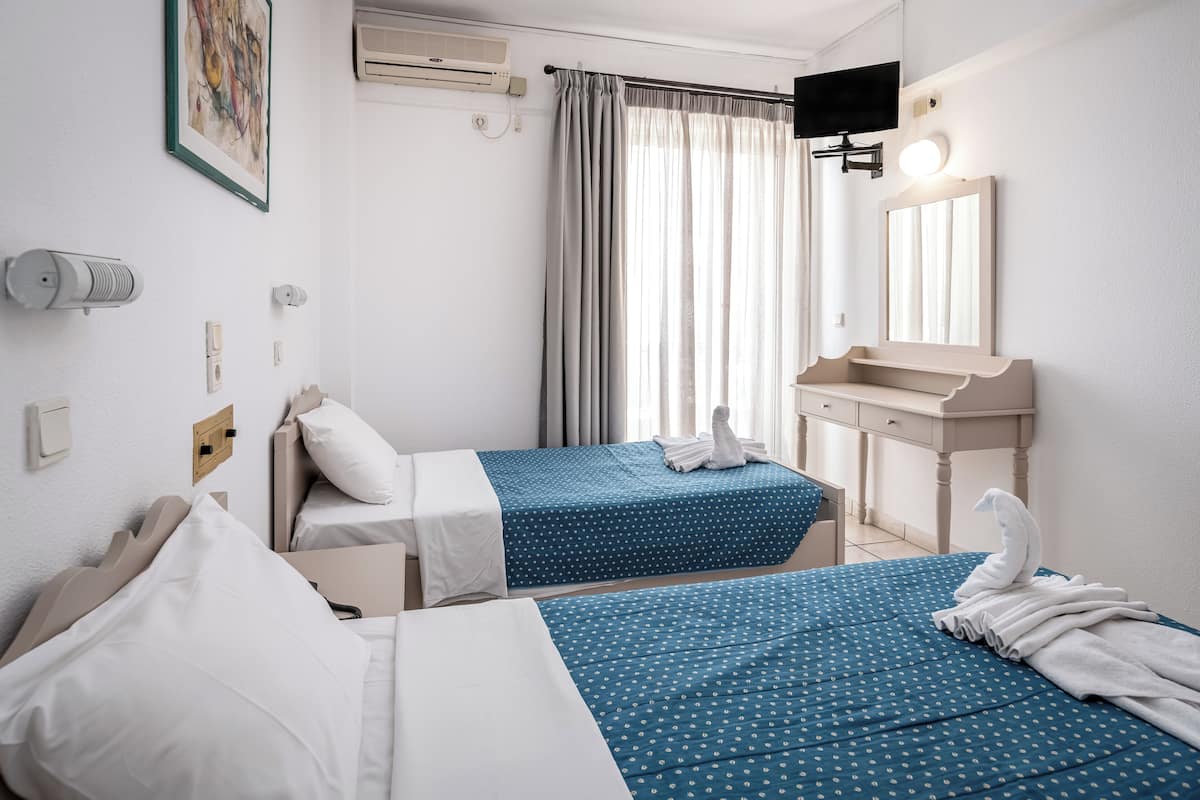 A hotel room with two beds, a bathroom with a sink and mirror, and a TV mounted on the wall.