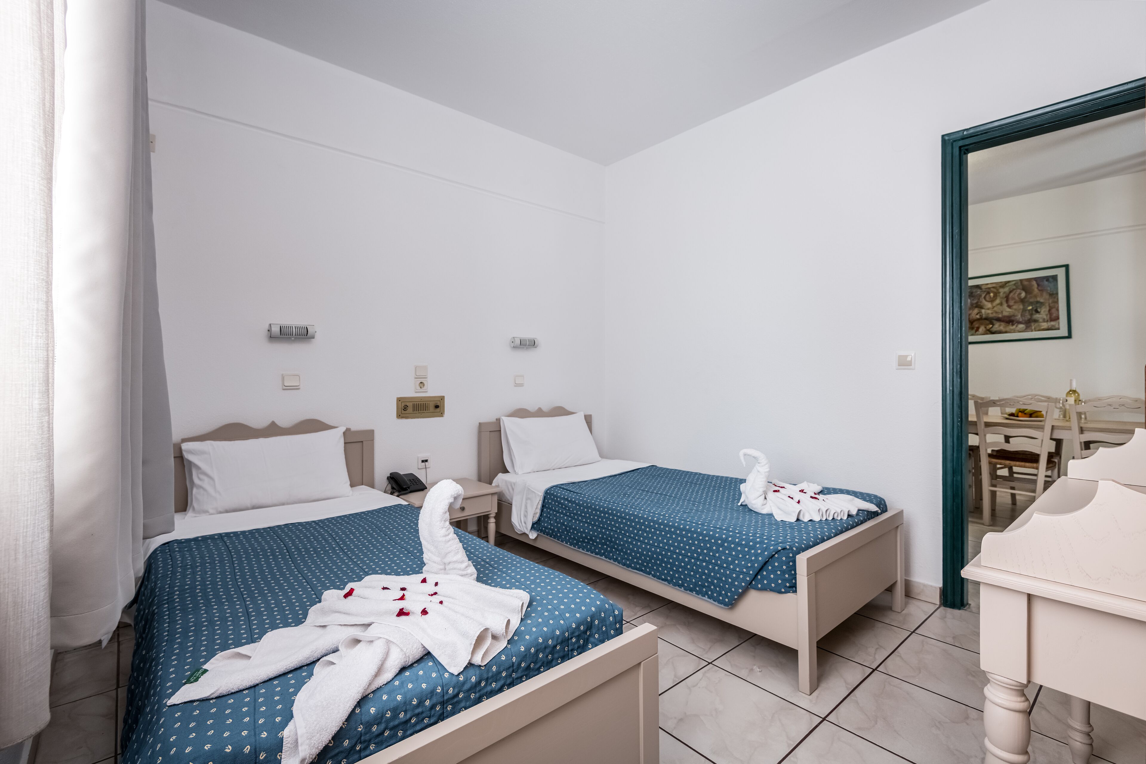A hotel room with two single beds, a small desk, and a chair.