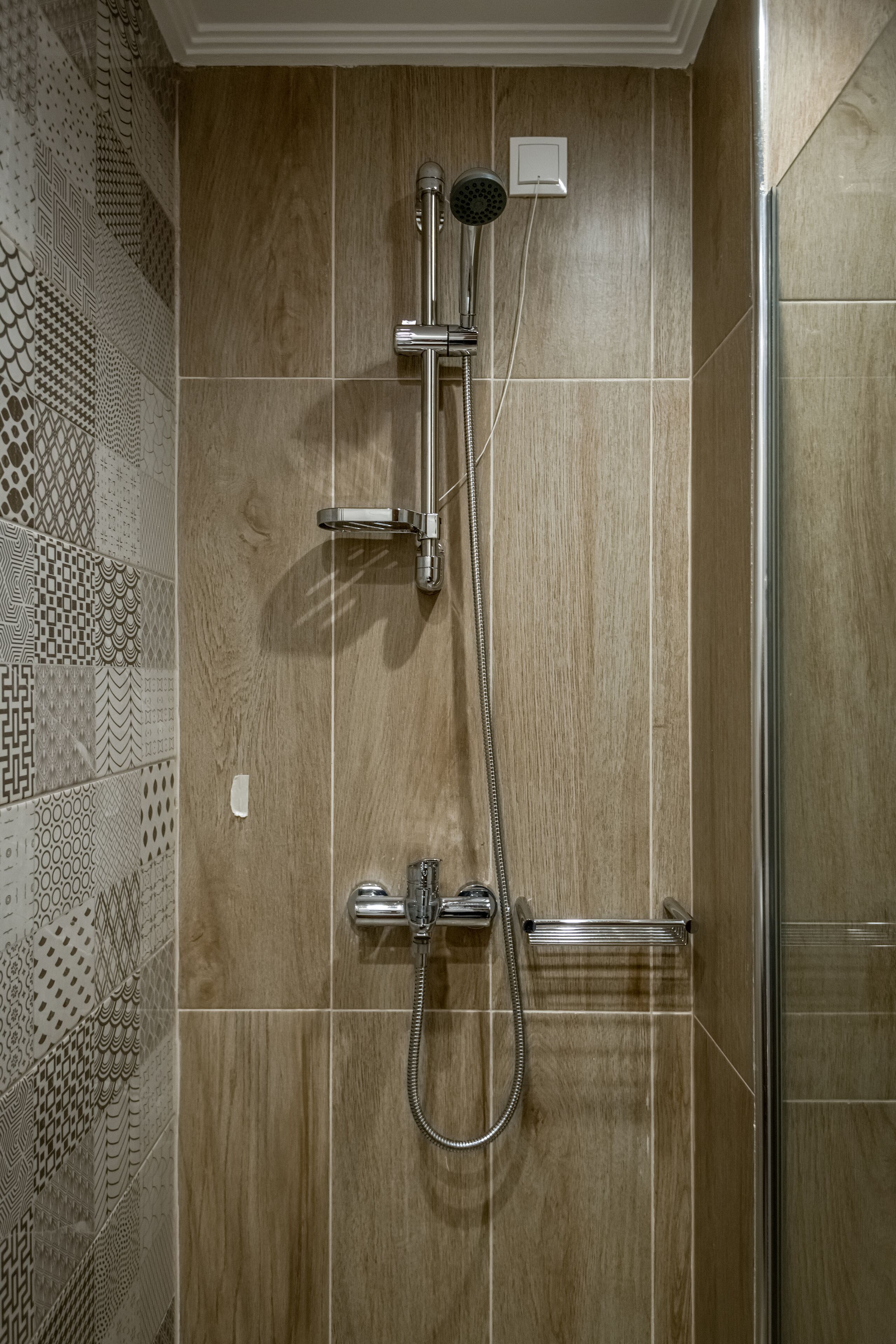 Eine Dusche mit Handbrause und fest installierter Duschköpfe, beide an einer Wand mit einem Musterfliesen-Design angebracht.