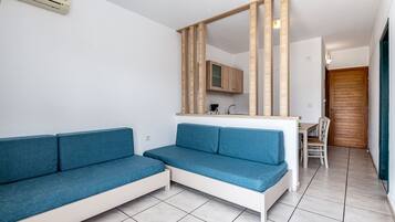 A modern living room with a blue sofa, a wooden-framed mirror, a kitchen area, and a wooden door.