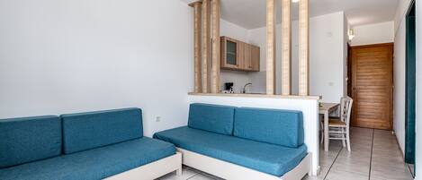 Un saló modern amb un sofà blau, un mirall amb marc de fusta, una zona de cuina i una porta de fusta.