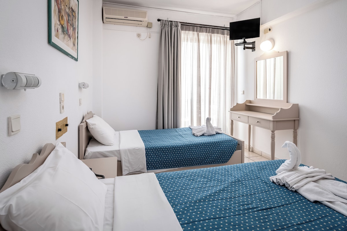 A hotel room with two beds, a bathroom, a TV, and a window with curtains.