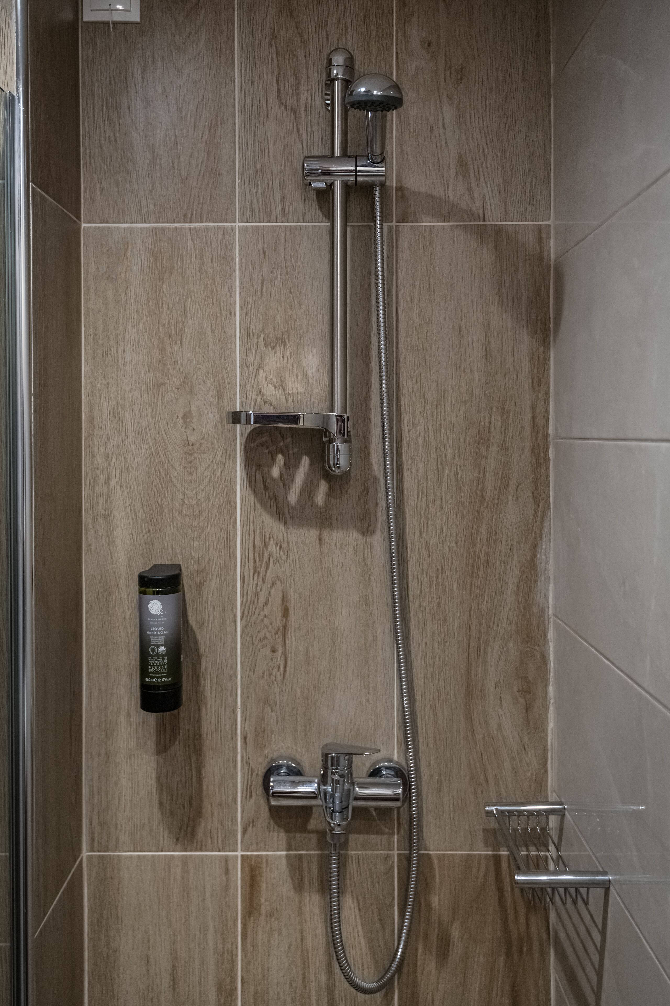 A shower with a handheld showerhead and a wall-mounted faucet, a soap dispenser, and a towel rack.