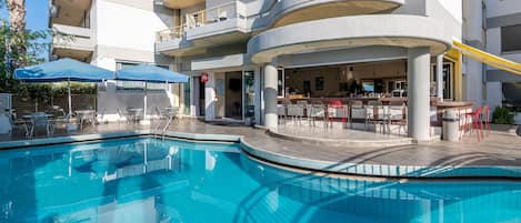 A modern hotel with a pool area, outdoor seating, and a bar.