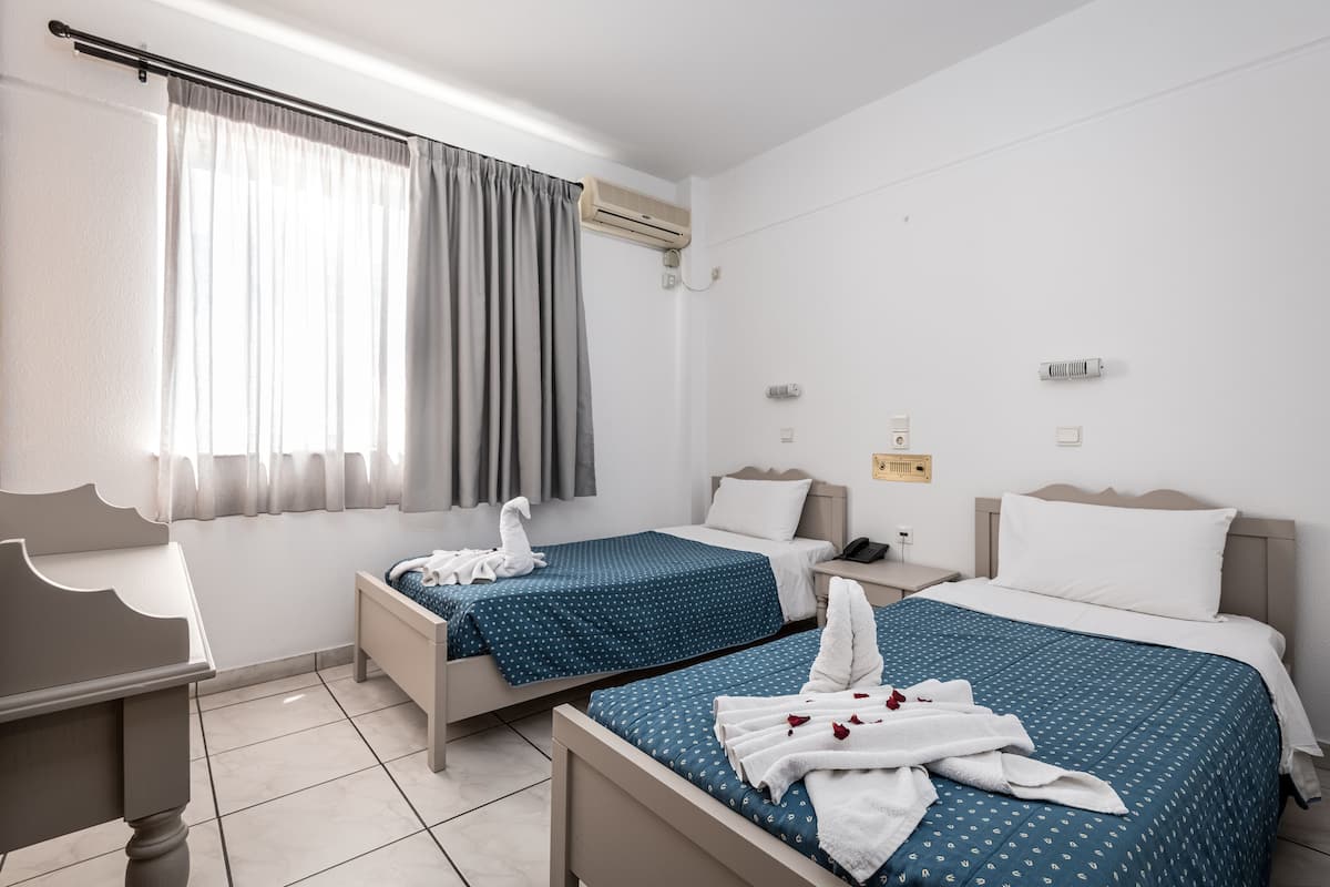 A hotel room with two beds, a desk, and a window with curtains.