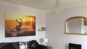 Un salon avec un canapé noir, un téléviseur, un lustre et un tableau représentant un cerf.