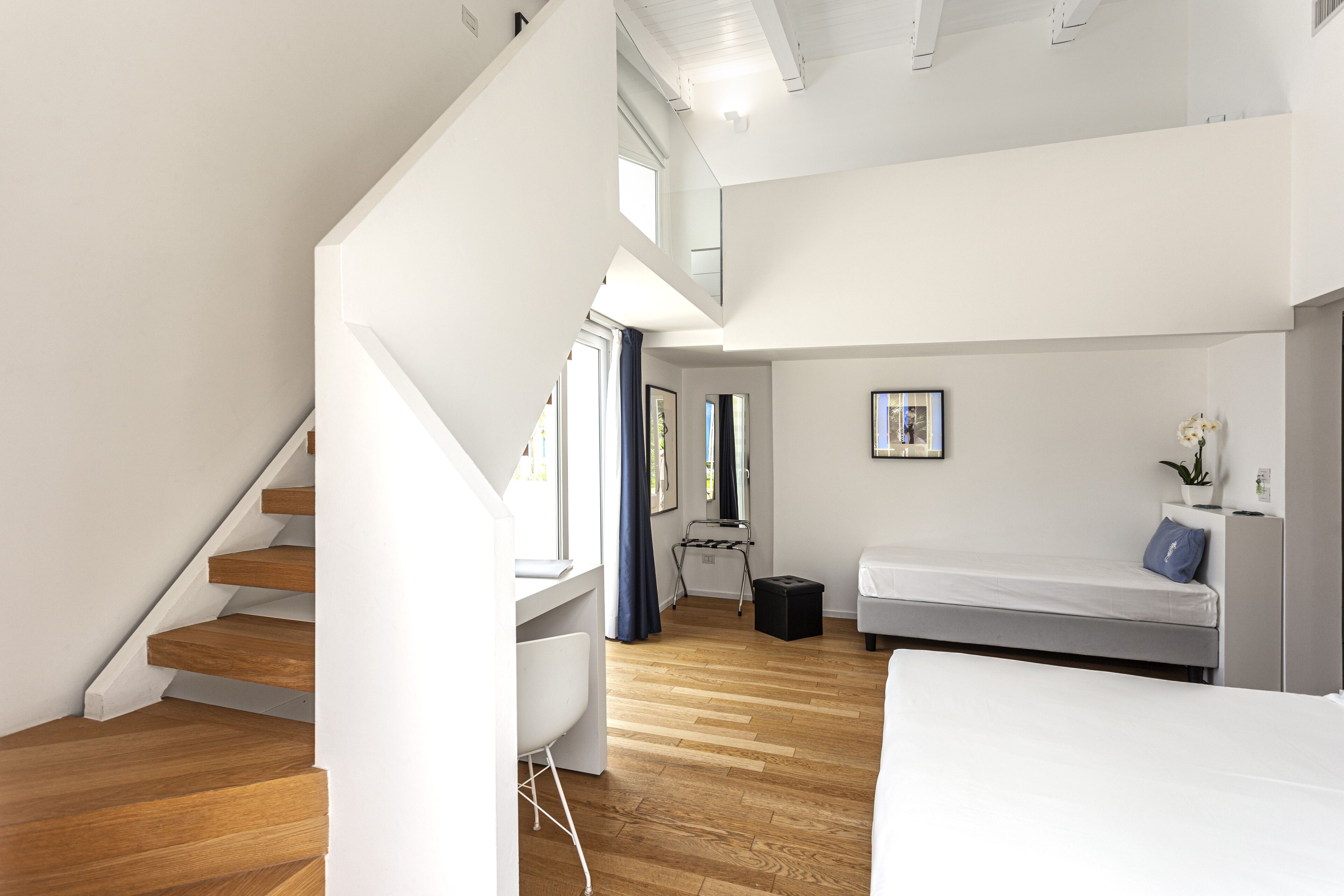 Un interior moderno con una escalera de madera, una cama, un escritorio y una ventana con cortinas.