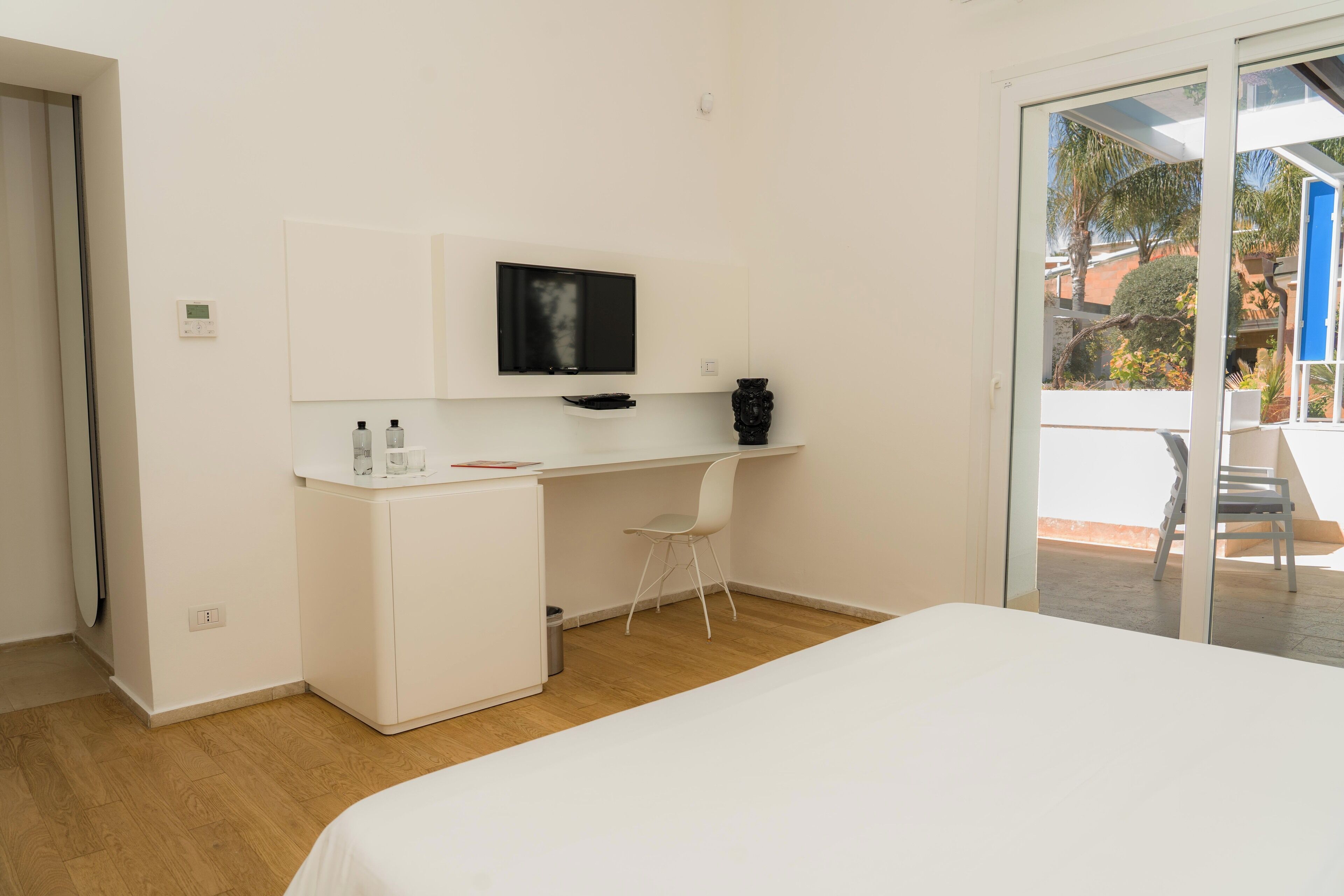 Un dormitorio con cama, un escritorio con televisor, una silla y un mueble pequeño.