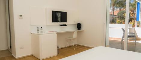 Un dormitorio con cama, un escritorio con televisor, una silla y un mueble pequeño.