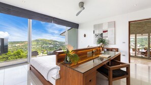A modern bedroom with a large bed, a wooden desk, and a view of a green landscape.