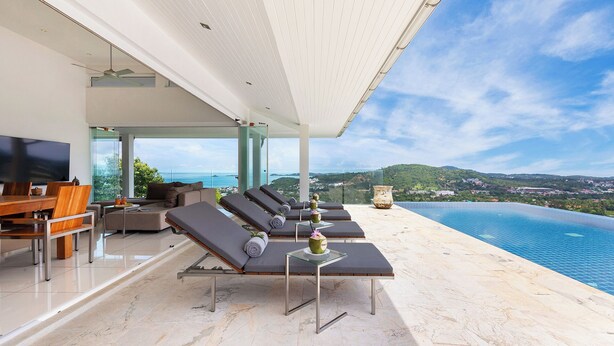 Un moderno espacio lounge al aire libre con piscina, tumbonas, una mesa de comedor y una pantalla de televisión.