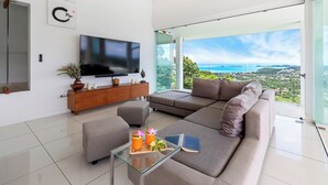 Una sala de estar moderna con un televisor de pantalla plana grande, un sofá, una mesa de centro de vidrio y vista al océano.