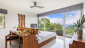 Un dormitorio moderno con una cama grande, un escritorio de madera, una televisión y vistas al océano.