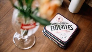 Une pile de dessous de verre de la brasserie Thwaites sur une table en bois.