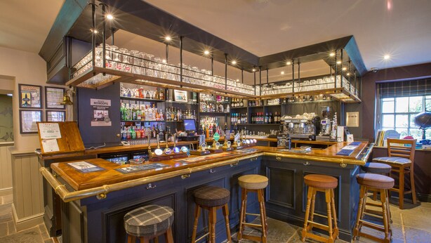 Un bar doté de nombreux tabourets, d’une grande variété de bouteilles et d’un intérieur bien éclairé.