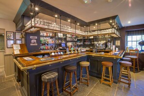 A bar with multiple stools, a variety of bottles, and a well-lit interior. - Howard Arms (Brampton)