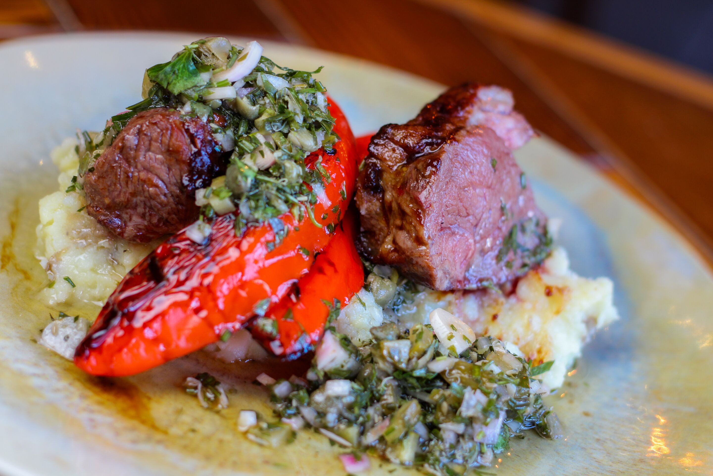 A plate with a piece of meat, a red vegetable, and a green herb topping.