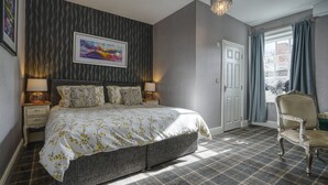 A bedroom with a large bed, two bedside tables, a chandelier, a door, and a window with curtains.