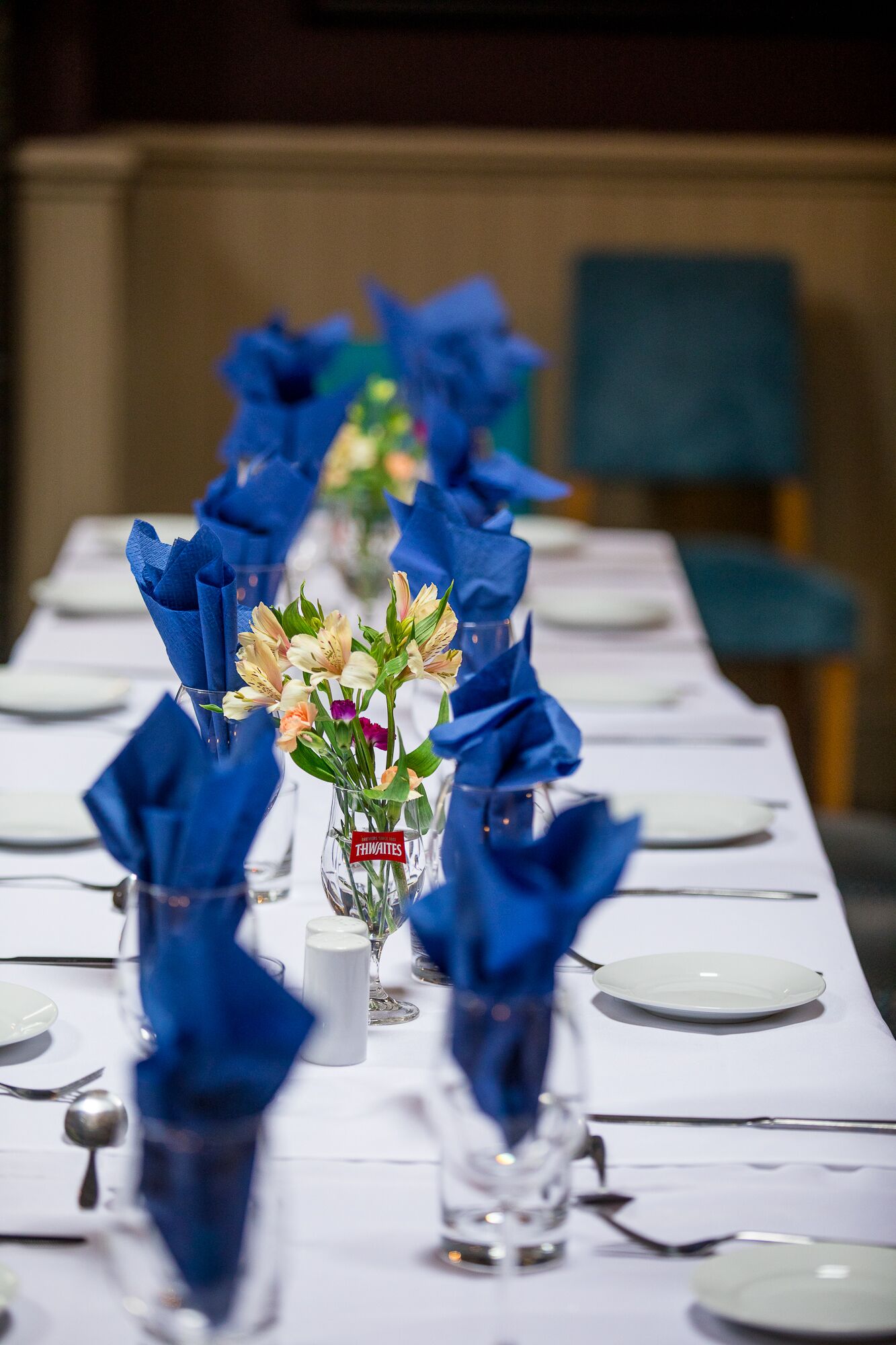 A dining table set with white plates, blue napkins, and glass vases with flowers.