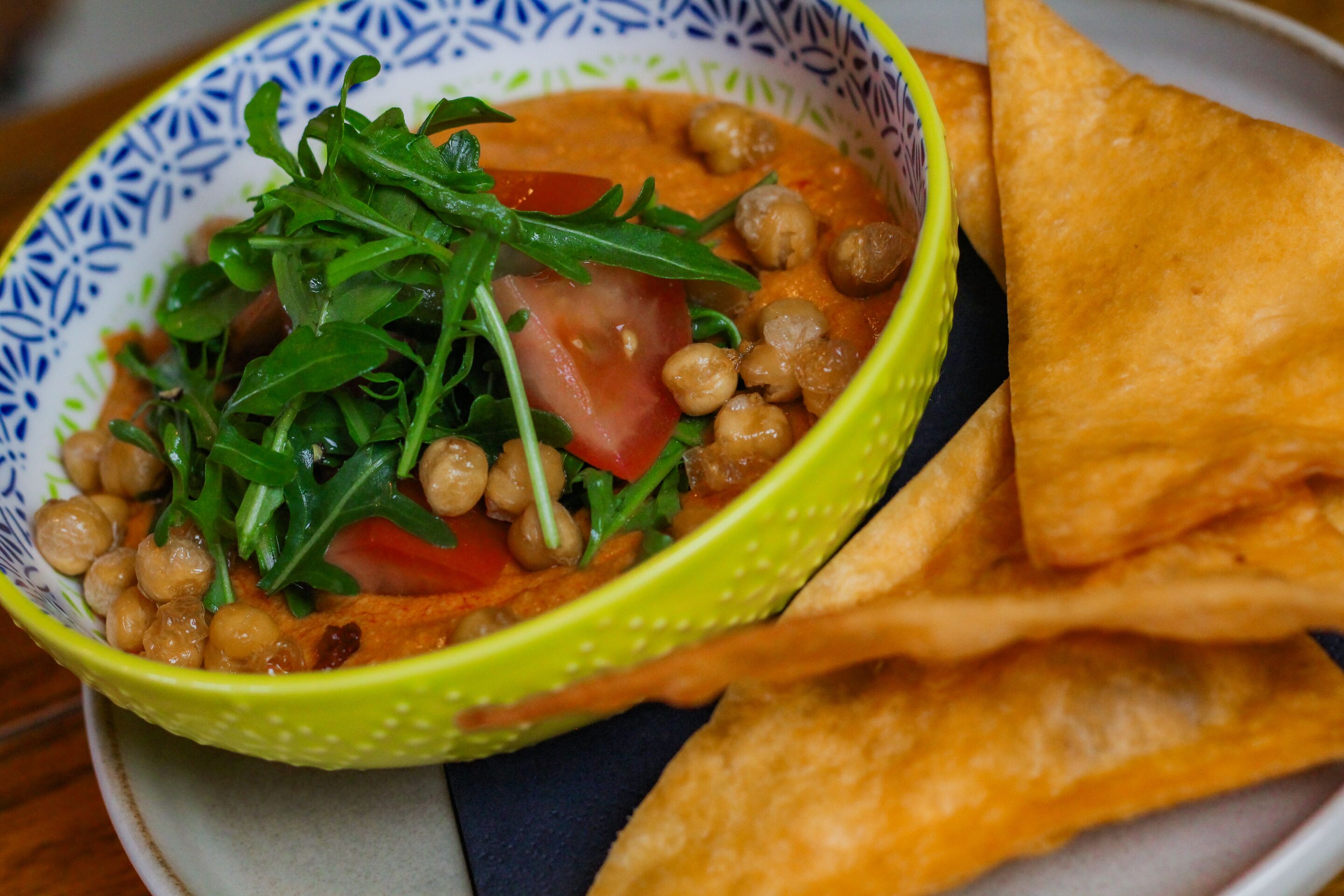 En skål suppe med kikærter, tomater og grønt, serveret med tortillachips.
