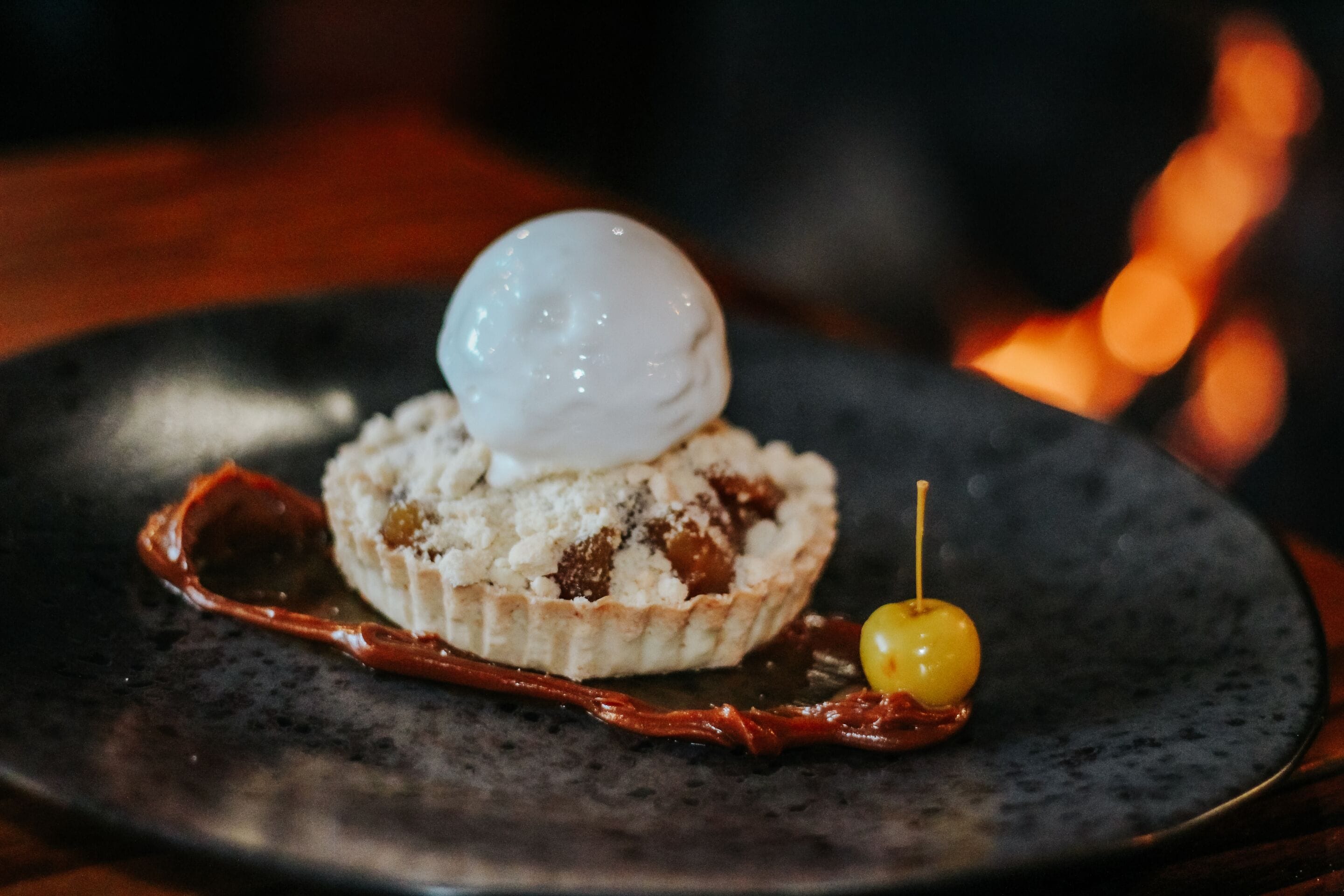 A dessert on a plate with a scoop of ice cream on top, a cherry, and a piece of what appears to be a caramelized fruit or candy.